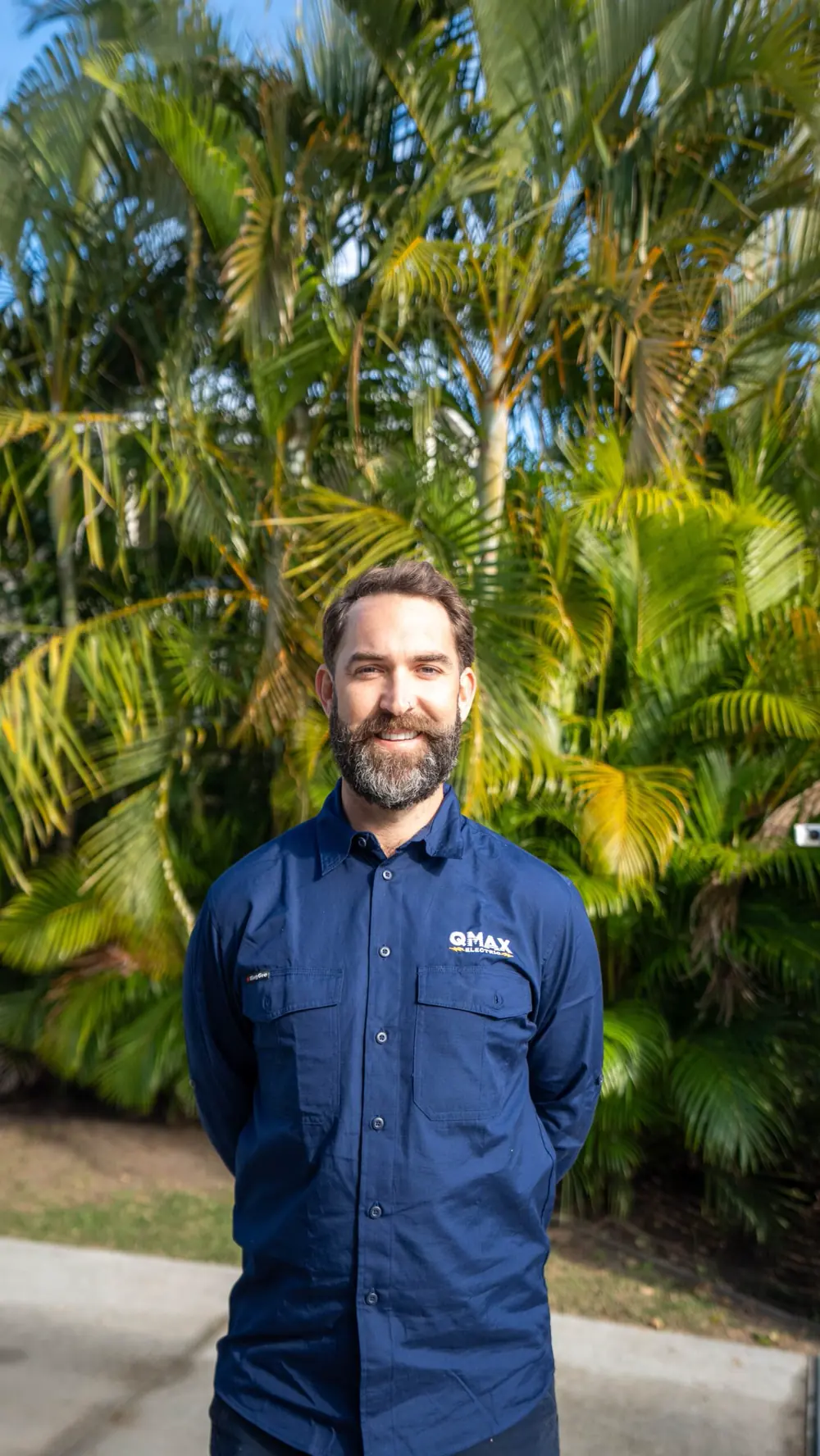 Mitch Eadie, director of QMAX Electric, in QMAX workwear in front of palms.