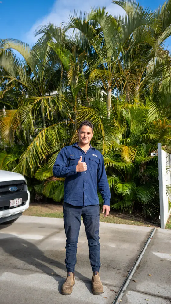 A young QMAX apprentice in navy workwear giving a thumbs up beside the ute.