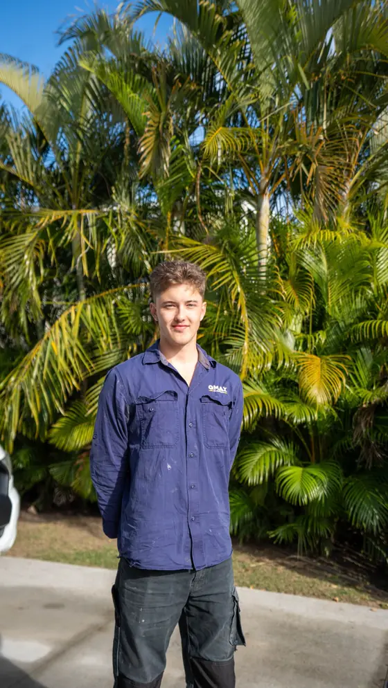 A QMAX electrician in navy workwear standing in front of palms.
