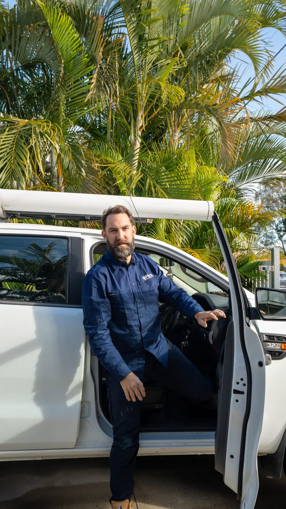 Mitch sitting in the open door of the white QMAX ute, smiling.