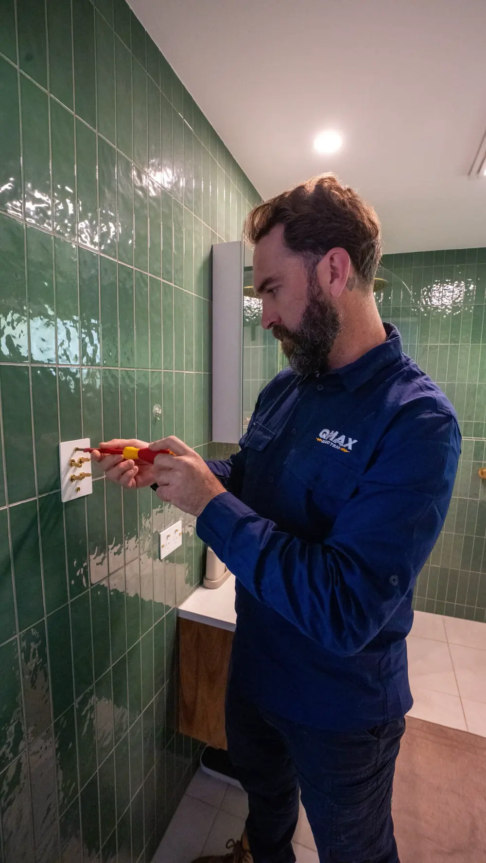 Mitch fitting a custom switch plate on a green-tiled bathroom wall.