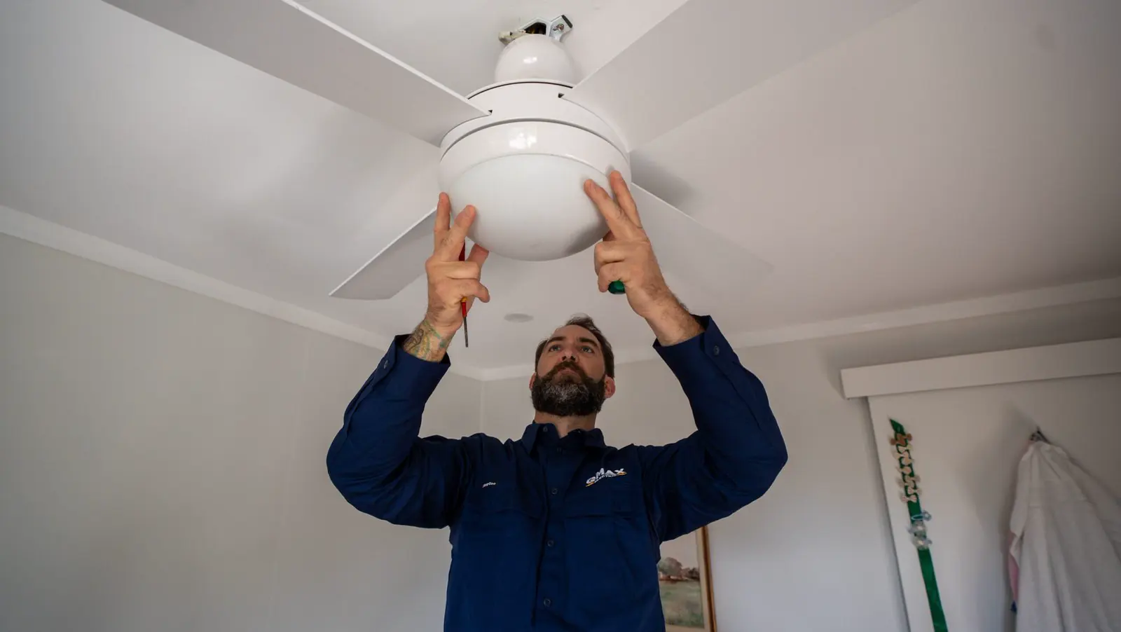 A QMAX electrician fitting a white ceiling fan.