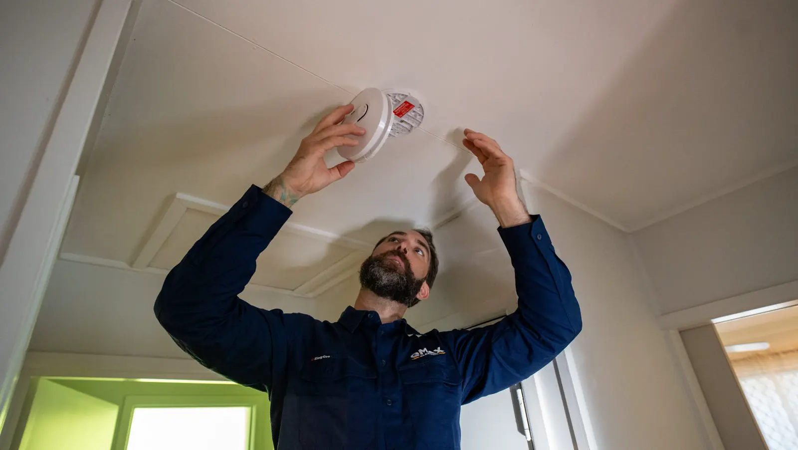 A QMAX electrician fitting a smoke alarm to a ceiling.