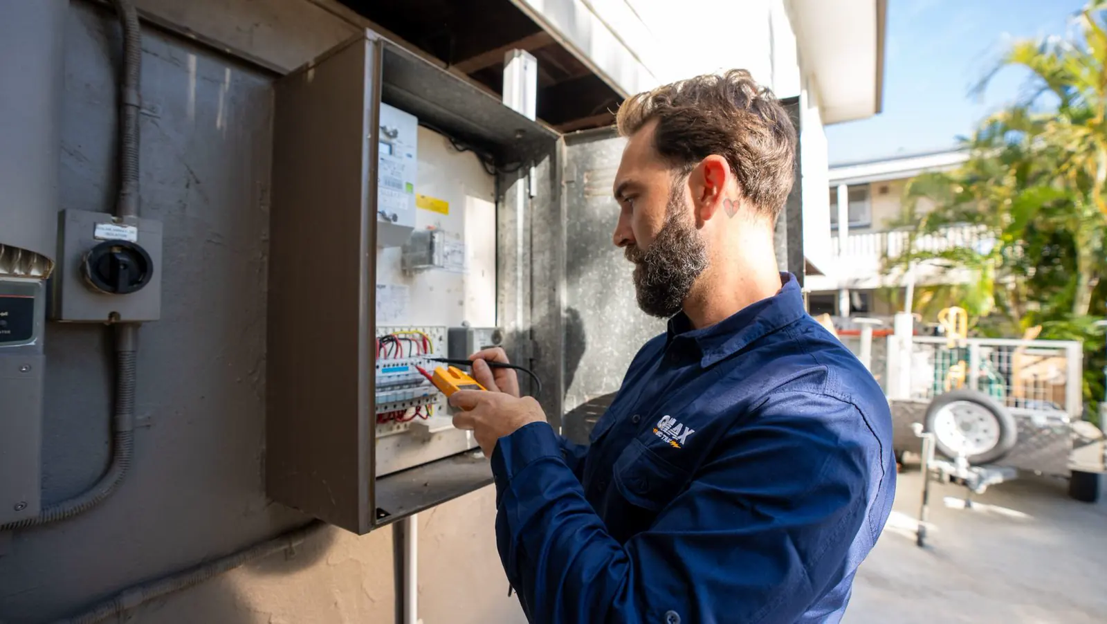 Mitch testing a switchboard with a multimeter on the side of a Brisbane house.